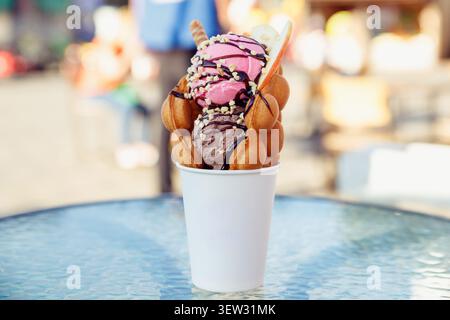 Belgische Waffel mit Eis in einer Pappbecher auf dem Glastisch des Straßencafés. Fastfood, süßes Sommeressen mitnehmen Stockfoto