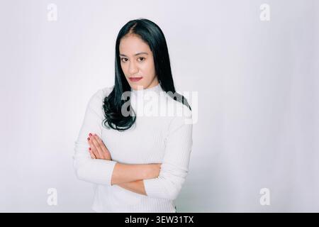 Ernsthafte asiatische Frau, die mit gekreuzten Armen auf weißem Hintergrund steht Stockfoto