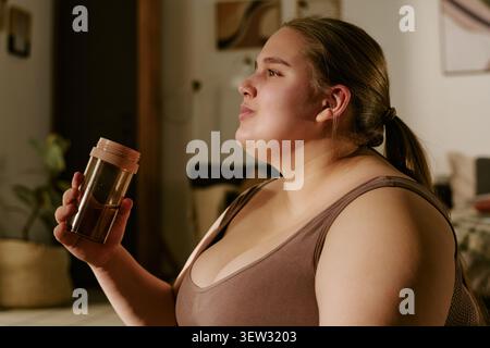 Plus Size Frau trinkt Wasser während der Wellness-Routine zu Hause Stockfoto