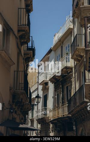 Die enge Straße der Altstadt mit traditionellen sizilianischen Barockfassaden verzierten Balkonen und einer alten Straßenlampe vor blauem Himmel in Sizilien Italien Stockfoto