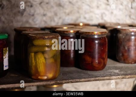 Reihen von Vintage-Glasbehältern mit fermentiertem Gemüse und konserviertem Obst, die auf einem Holzregal in einem Steinkeller gelagert sind und Gefühle von se wecken Stockfoto