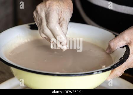 Nahaufnahme der Hände, die mit fermentiertem Sauerteig in einer Retro-Schüssel arbeiten, um die Textur und Konsistenz zu zeigen, die für handgemachtes Brot, Celebratin, erforderlich sind Stockfoto