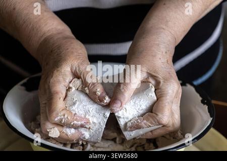 Reife Hände zerbröckeln die rohe Hefekultur in eine Metallschale und betonen die authentische kulinarische Praxis und die haptische Zubereitung von Sauerteigbrot mit Stockfoto