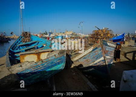 Zwei alte, verwitterte blaue Fischerboote ruhen an Land im Hafen von Essaouira in Marokko, mit Stapeln von Hummertöpfen und anderen Booten, die im Backgr zu sehen sind Stockfoto