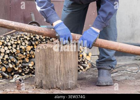 Person in Arbeitsuniform hält ein schweres Stahlrohr fest gegen einen Holzfuß, um das Schneiden vorzubereiten, und hebt handwerkliches Können und Baugewerbe hervor Stockfoto