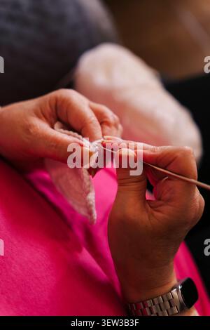 Hände häkeln ein weißes Garnstück mit Häkelnadel nah oben. Slow Living und Textilkunstkonzepte. Stockfoto