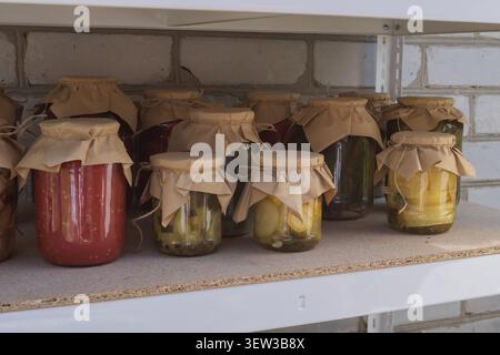 Traditionelle hausgemachte Konfitüren in Glasgläsern, die in Regalen der Speisekammer gelagert werden. Eingelegtes Gemüse, Tomaten und Pilze bereit für den Winter. Stockfoto