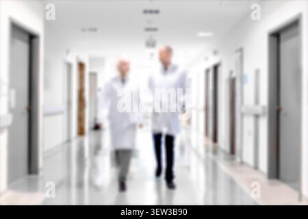 Unscharfer Hintergrund von Ärzten und Krankenpflegern, die in einem Krankenhausflur gehen. Unscharf fokussierte Gesundheitsfachkräfte in Bewegung entlang eines Klinikflurs. Stockfoto