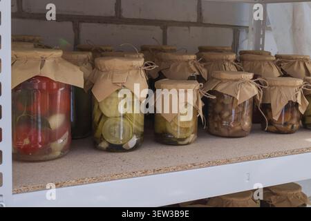 Traditionelle hausgemachte Konfitüren in Glasgläsern, die in Regalen der Speisekammer gelagert werden. Eingelegtes Gemüse, Tomaten und Pilze bereit für den Winter. Stockfoto