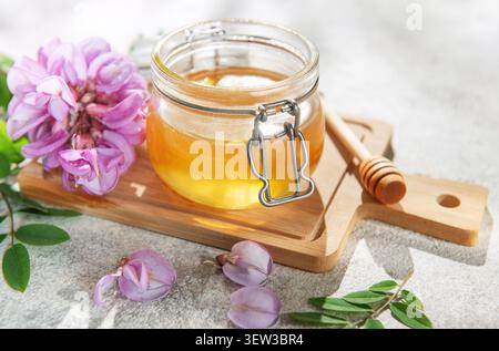 Honig in einem Glas mit rosa Akazienblüten und einem Holzlöffel auf einem Brett Stockfoto