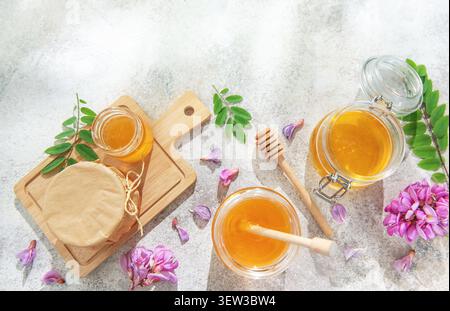 Honiggläser mit Löffeln, frische Akazienblüten und Blätter auf hellem Hintergrund Stockfoto