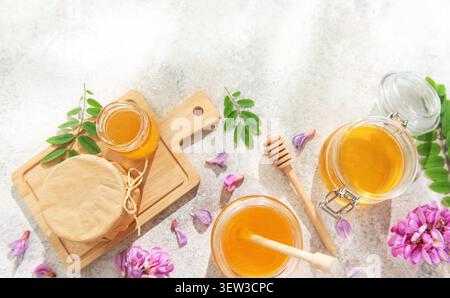 Honiggläser mit Löffeln, frische Akazienblüten und Blätter auf hellem Hintergrund Stockfoto