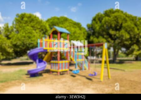 Unscharfer farbenfroher Außenspielplatz mit Rutsche und Schaukel in einem Park. Kinderferienhaus umgeben von Bäumen für die Freizeit der Familie. Stockfoto