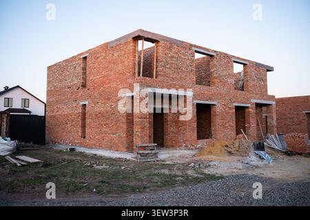 Ein Weitwinkelblick auf ein modernes, zweistöckiges Haus, das sich im Bau befindet, aus roten Tonziegeln gebaut, mit offenen Fenstern und Türrahmen Stockfoto