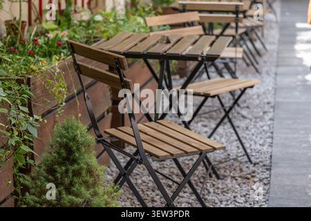 Gemütliche Terrasse im Freien mit Holztischen und Stühlen, umgeben von Grün in einem europäischen Stadtviertel. Das Bild repräsentiert Gastfreundschaft im Freien Stockfoto