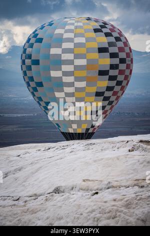 Ein großer Heißluftballon mit einem leuchtenden blauen, gelben, schwarzen und roten Karomuster wird während des Fluges über dem charakteristischen weißen Travertin erfasst Stockfoto