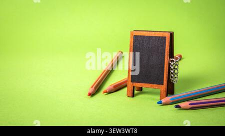 Leeres Schwarzes Tafel mit farbigen Bleistiften auf grünem Hintergrund für sauberen Kopierraum Stockfoto