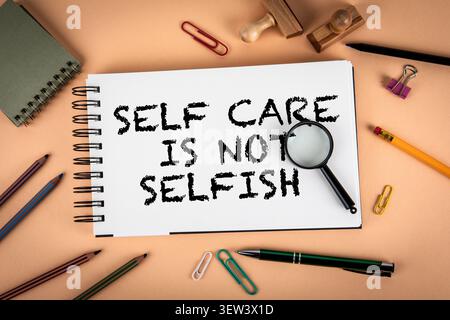 Motivationsphrase Self Care ist nicht selbstsüchtig geschrieben auf Notizbüchern mit Bürowerkzeugen Stockfoto