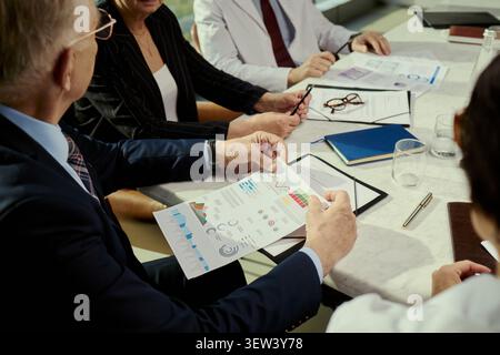 Leitender Geschäftsmann, der den Analysebericht mit Kollegen während des Meetings überprüft und Strategie- und Leistungskennzahlen bespricht. Nützlich für Unternehmensplanung, Finanzen und Teamwork-Kampagnen Stockfoto