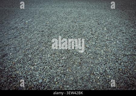 Eine riesige Fläche aus glatten, dunkelgrauen und bläulichen Kieselsteinen bedeckt den Boden und erstreckt sich zu einem gedämpften Horizont. Die einheitliche, aber unterschiedliche Textur dieser Stockfoto