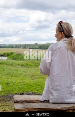 Frau mittleren Alters sitzt draußen und blickt während eines Picknickausflugs über die Landschaft. Ruhige Kontemplation, Entspannung und friedliche Anbindung Stockfoto
