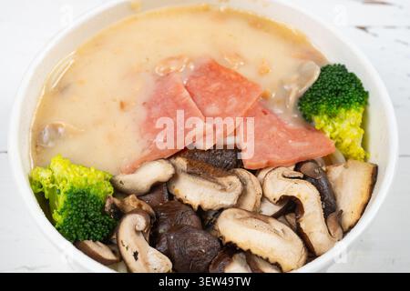 Schüssel mit cremigen Pilzen und Specknudeln, mit reichhaltiger, samtiger Sauce, frischen gemischten Pilzen, herzhaften Speckscheiben, und lebendiger Brokkoli fl Stockfoto