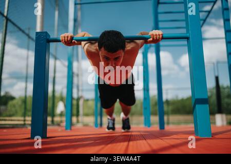 Sportlicher Mann, der während des täglichen Workouts auf Calisthenics-Bars mit Steigungen Liegestütze ausführt Stockfoto