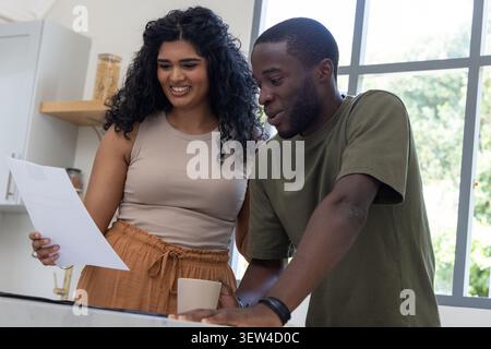 Diverse Paare, die Dokumente an der Küchentheke lesen, Frau mit Papier, Keramikbecher in der Nähe Stockfoto