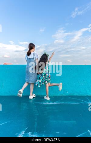 Zwei Mädchen, die auf einer blauen Wand stehen, schauen auf Distanz, Freundschaft und Neugier Stockfoto