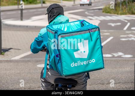 Deliveroo Fahrradkurier fährt entlang einer Straße. Deliveroo ist ein britisches multinationales Online-Lebensmittellieferunternehmen Stockfoto