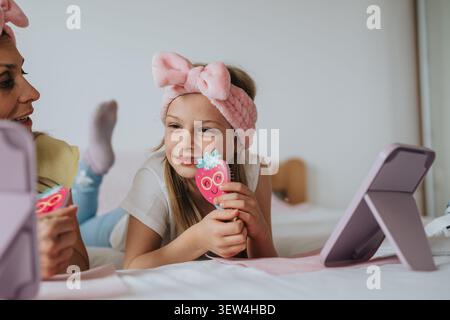 Mutter und Kind genießen einen verspielten Heim-Spa-Moment mit Spiegel und Spielzeugbürste auf dem Bett Stockfoto