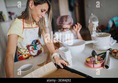 Mama und Kind backen zusammen in einer hellen Küche mit einem Geburtstagskuchen in der Nähe Stockfoto