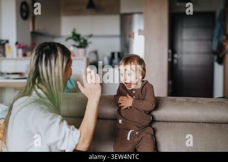 Mama und Kleinkind teilen sich fröhliche High Five auf dem Sofa in einem gemütlichen Wohnzimmer zu Hause Stockfoto
