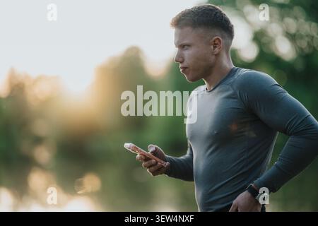 Ein junger Mann, der sein Smartphone benutzt, nachdem er zur goldenen Stunde am See gelaufen ist Stockfoto