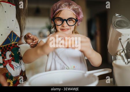 Mutter und Tochter backen zusammen in einer Küche, während das Kind ein Ei in eine Schüssel knackt Stockfoto