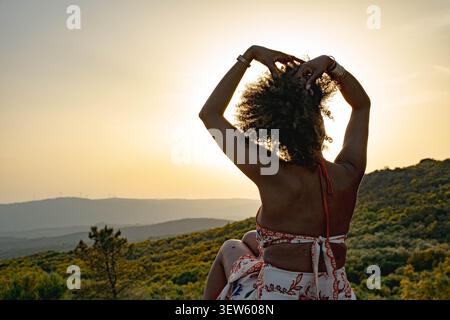 Frau mit lockigem Haar posiert auf einem Hügel bei Sonnenuntergang Stockfoto