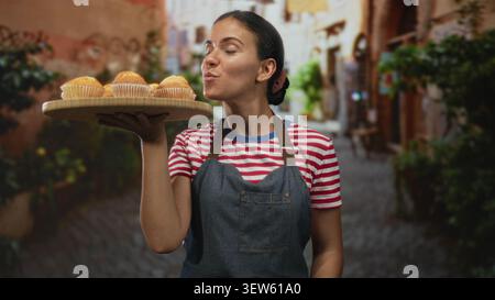 Frau mit hölzernem Tablett von Muffins auf erhobener Hand in einem kopfsteingepflasterten Straßenmarkt; Gastfreundschaft kleines Geschäft. Stockfoto