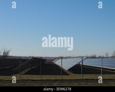 Reihen blauer Photovoltaikpaneele sind in einem offenen, grünen Raum unter klarem Himmel installiert. Die Solarpaneele erzeugen saubere, alternative Energie. Stockfoto