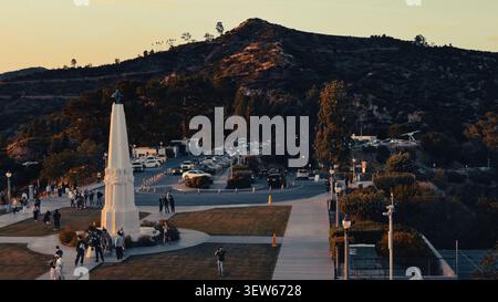 Touristen treffen sich am Astronomers Monument am Griffith Observatory mit Mount Hollywood im Hintergrund während des Sonnenuntergangs in Los Angeles. Stockfoto