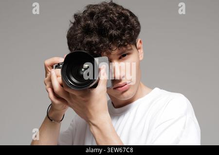 Ein junger, männlicher Fotograf fokussiert sich auf seine Kamera, die bereit ist, atemberaubende Bilder in einem Studio aufzunehmen und seine professionellen Fähigkeiten und sein modernes e zu demonstrieren Stockfoto
