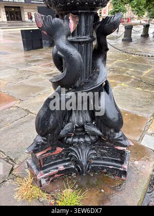 Ein verwitterter gusseiserner Schiffspoller im viktorianischen Stil mit skulpturalen Delfinmotiven auf einer gepflasterten Straße in Liverpool, Großbritannien. Stockfoto