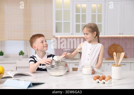 Bruder und Schwester machen Teig am weißen Marmortisch in der Küche Stockfoto