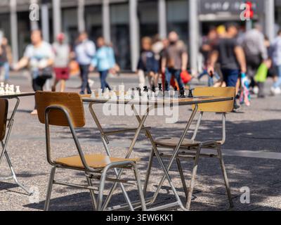 Das Schachbrett wartet auf Spieler in einer städtischen Straße mit Stühlen und unscharfen Menschen, die im Hintergrund laufen Stockfoto