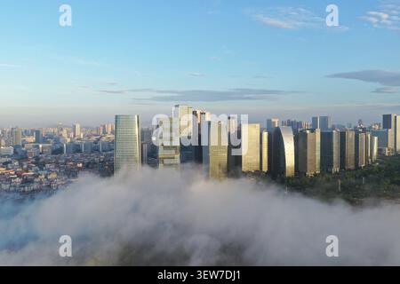 Ein Drohnenfoto zeigt eine Reihe unterschiedlicher moderner Wolkenkratzer mit verschiedenen architektonischen Formen, die über einer Wolkendecke in Xiamen ragen, deren Glas und Stockfoto