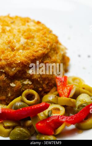 Goldenes gebratenes Patty sitzt auf weißem Teller. Rote Paprika und grüne Oliven sorgen für einen lebendigen Kontrast. Helle Farben deuten auf frische, gesunde Mahlzeit Option. Einfache PR Stockfoto