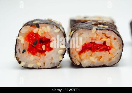 In zwei Hälften geschnittene Sushi-Rolle mit roter Füllung. Weißer Reis, schwarzer Sesam und weißer Sesam sind sichtbar. Algenverpackung umhüllt den Cent der Rolle Stockfoto