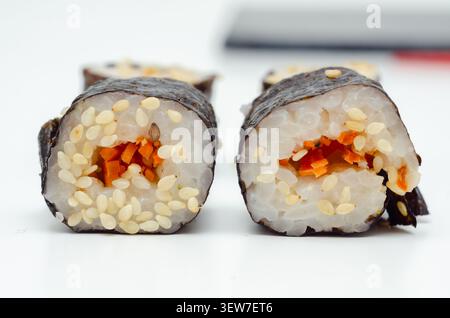 In zwei Hälften geschnittene Sushi-Rolle mit roter Füllung. Weißer Reis, schwarzer Sesam und weißer Sesam sind sichtbar. Algenverpackung umhüllt den Cent der Rolle Stockfoto