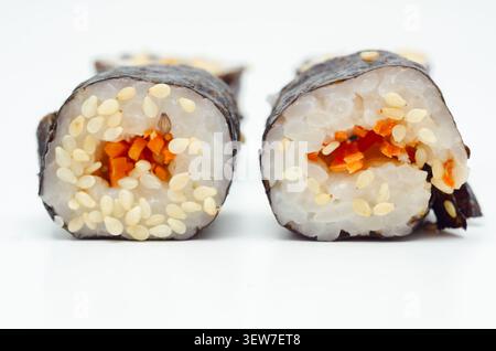 In zwei Hälften geschnittene Sushi-Rolle mit roter Füllung. Weißer Reis, schwarzer Sesam und weißer Sesam sind sichtbar. Algenverpackung umhüllt den Cent der Rolle Stockfoto