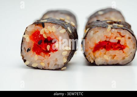 In zwei Hälften geschnittene Sushi-Rolle mit roter Füllung. Weißer Reis, schwarzer Sesam und weißer Sesam sind sichtbar. Algenverpackung umhüllt den Cent der Rolle Stockfoto