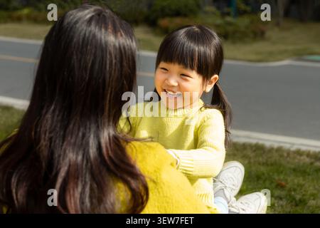 Liebevolle asiatische Mutter und Tochter sitzen auf Gras und lachen zusammen, emotionale Verbindung und Familienglücklich. Stockfoto